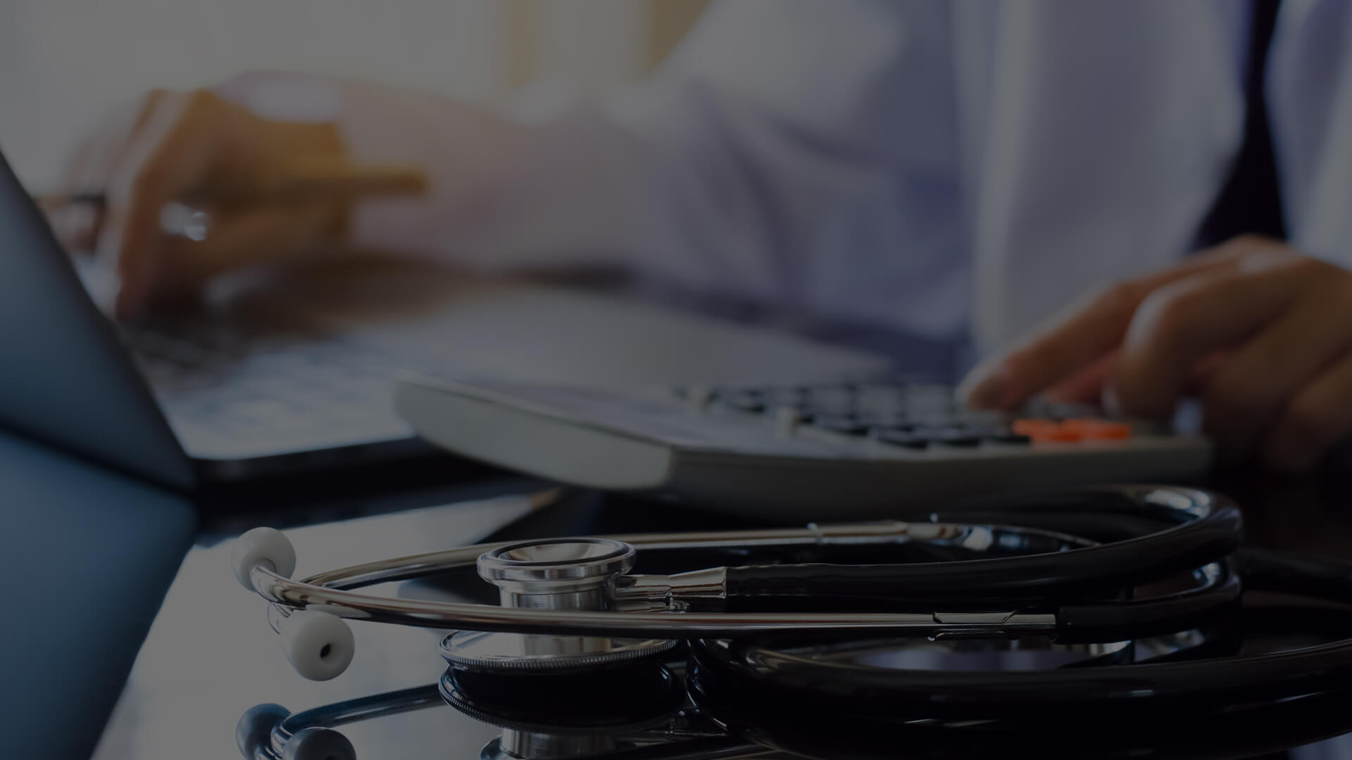 Revenue Integrity in Healthcare: Strategic Approach Doctor working on a laptop with a calculator and a stethoscope on the desk, illustrating the importance of revenue integrity in healthcare.