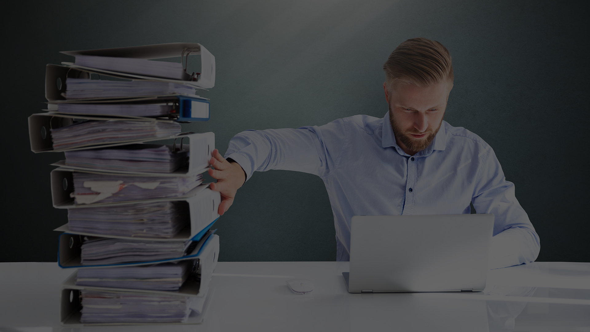 Man looks at computer while pushing a large stack of binders away