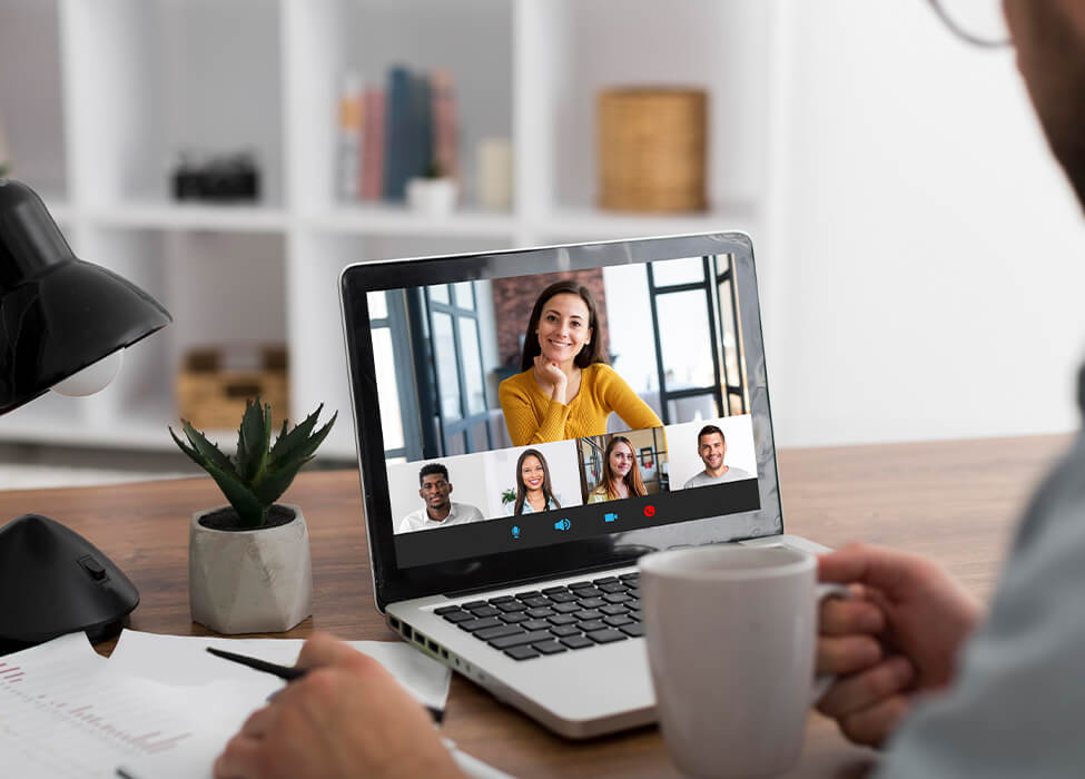 Person holding a mug of coffee while on a virtual meeting on his laptop