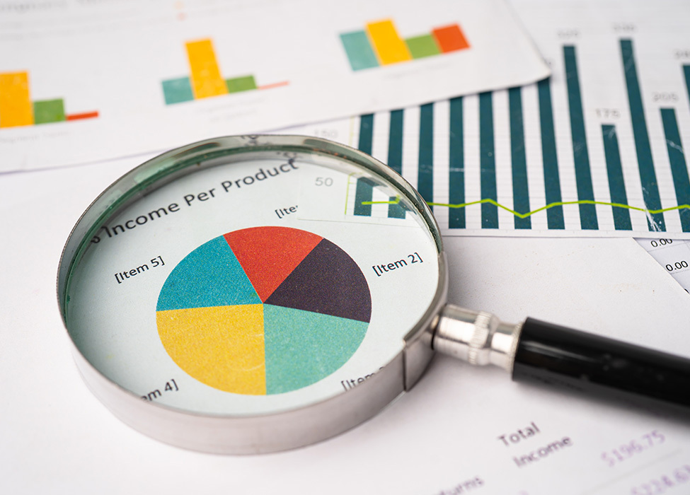 Scattered papers with graphs on them and a magnifying glass resting on top of one of the papers. 