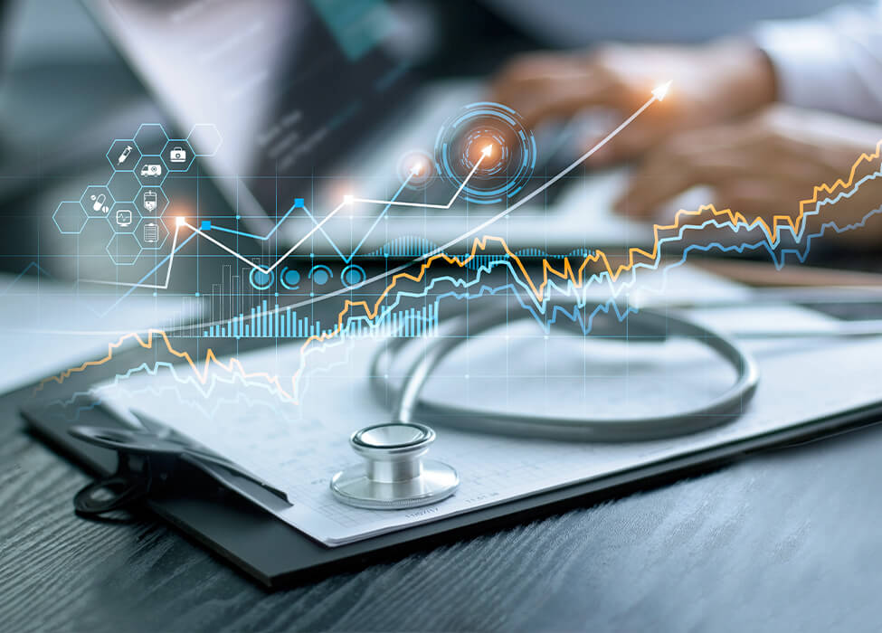 A stethoscope sits on a clipboard while a provider types on a laptop in the background