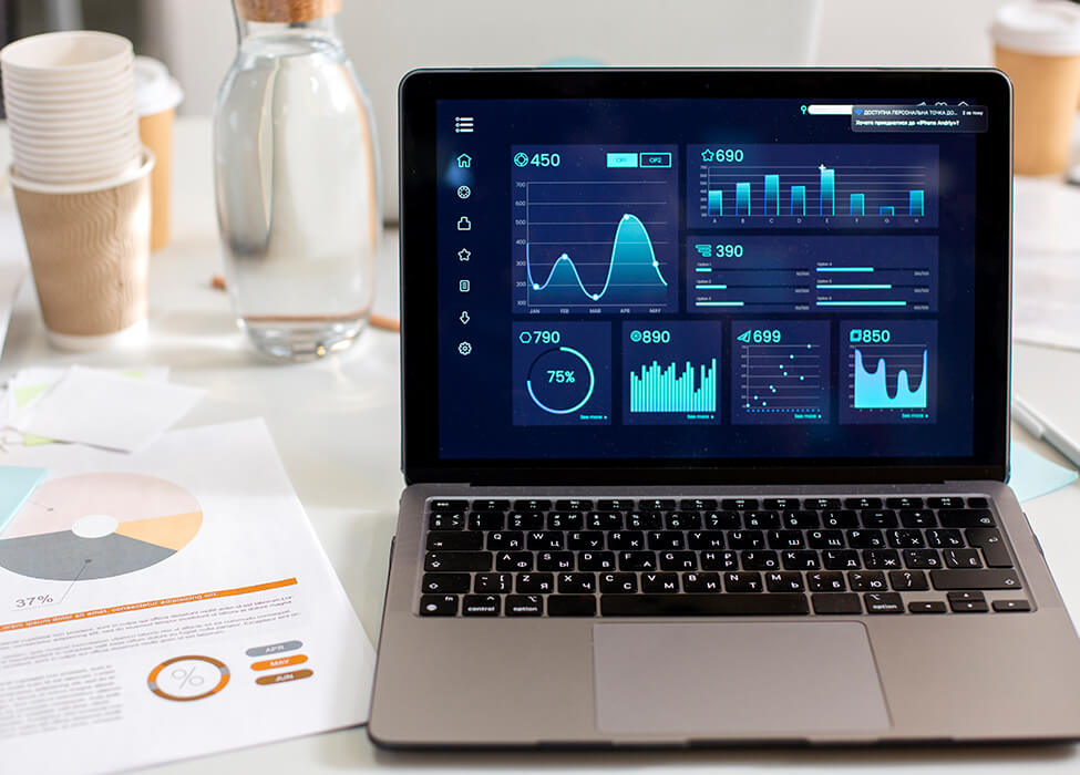 An open laptop on a desk showing a detailed analytics dashboard with various charts and graphs indicating business performance metrics