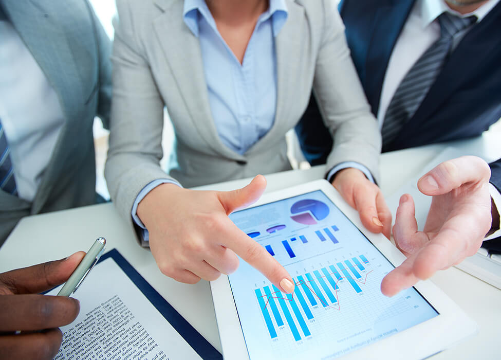 Close up of three professionals looking at a tablet with graphs on it