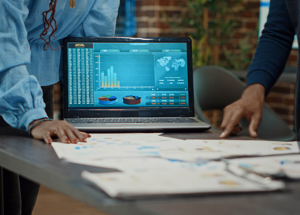 Professionals handling papers on a table while a laptop faces the camera with an image of a graph on it