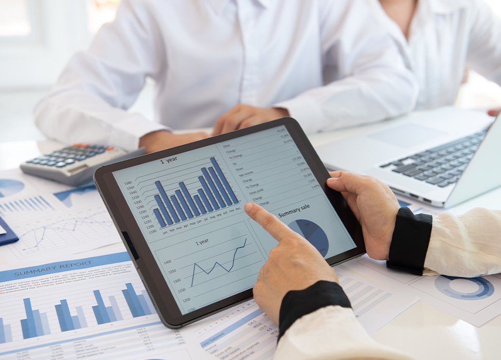 Financial Management Software | Image of three people at work sitting around a table with charts scattered around; one person holds a tablet.