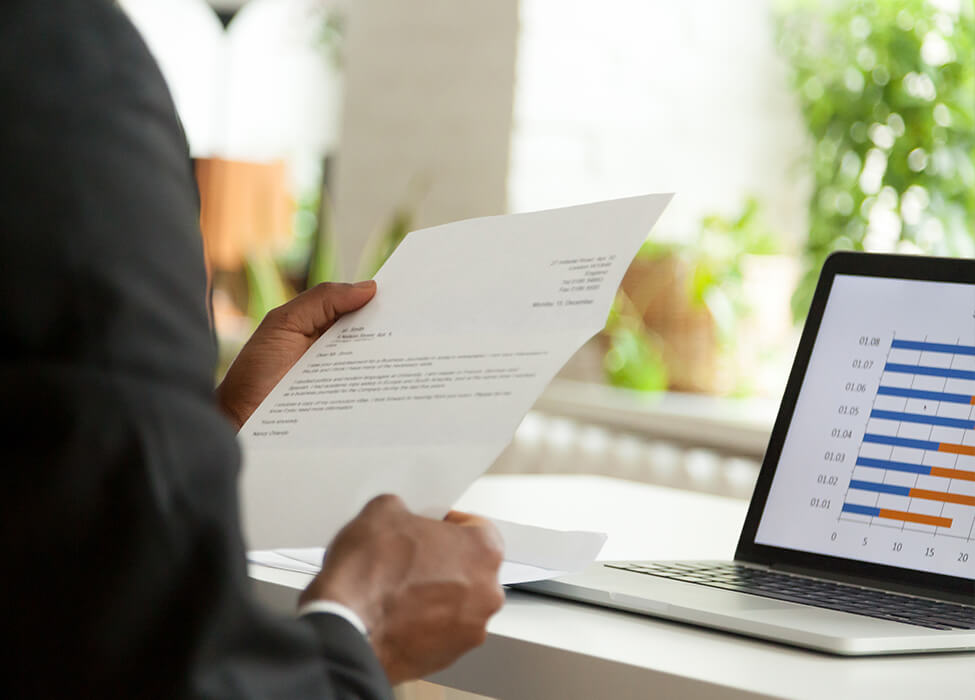 Man sitting at his desk with a laptop while he looks at a letter