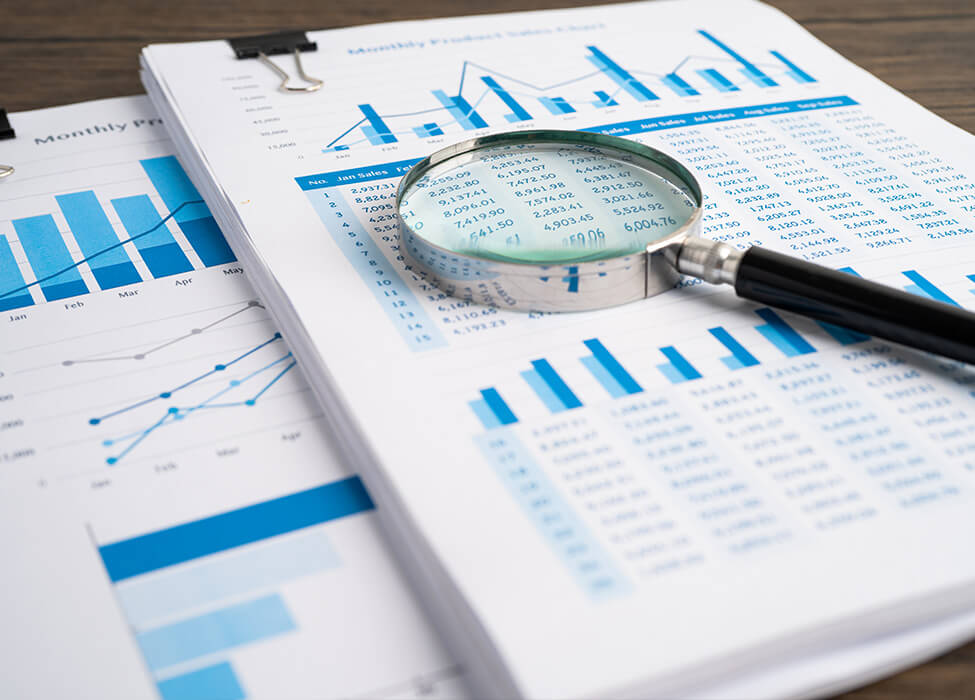 Papers with graphs resting on the table and a magnifying glass resting on the papers