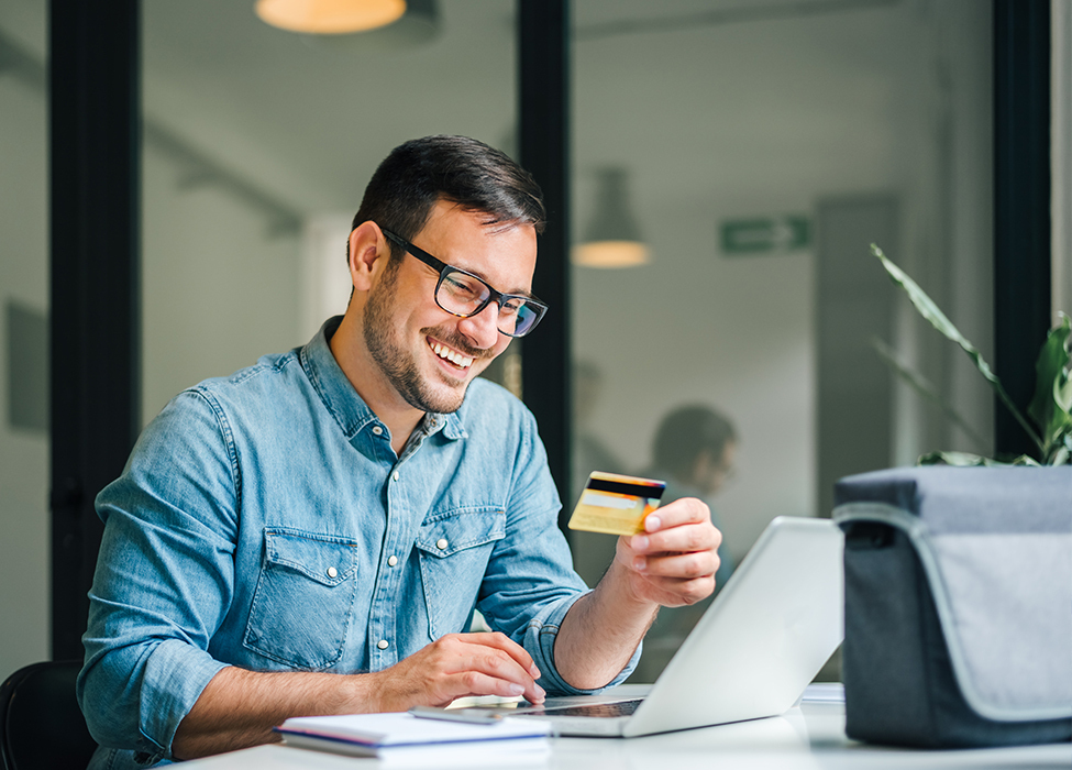 realtime payments | smiling man holding credit card while looking at his laptop