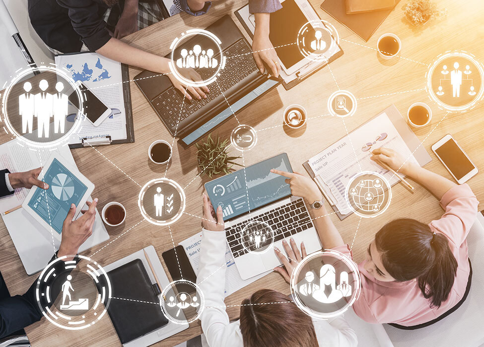 Business Process Automation: bird's eye view of people in business attire working on laptops at a table with icons floating above them