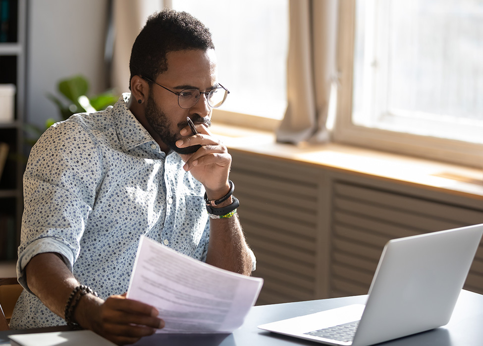 Paper Digitization: Man holds paper in one hand while working on his laptop with the other