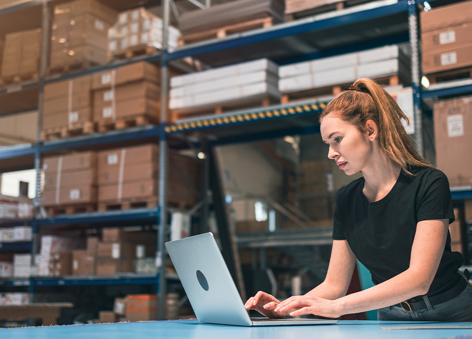 In a warehouse with boxes on the shelves, a person works on their laptop